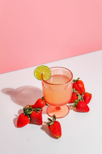Chilled strawberry lime drink in a pink glass surrounded by fresh strawberries, perfect for summer refreshment.