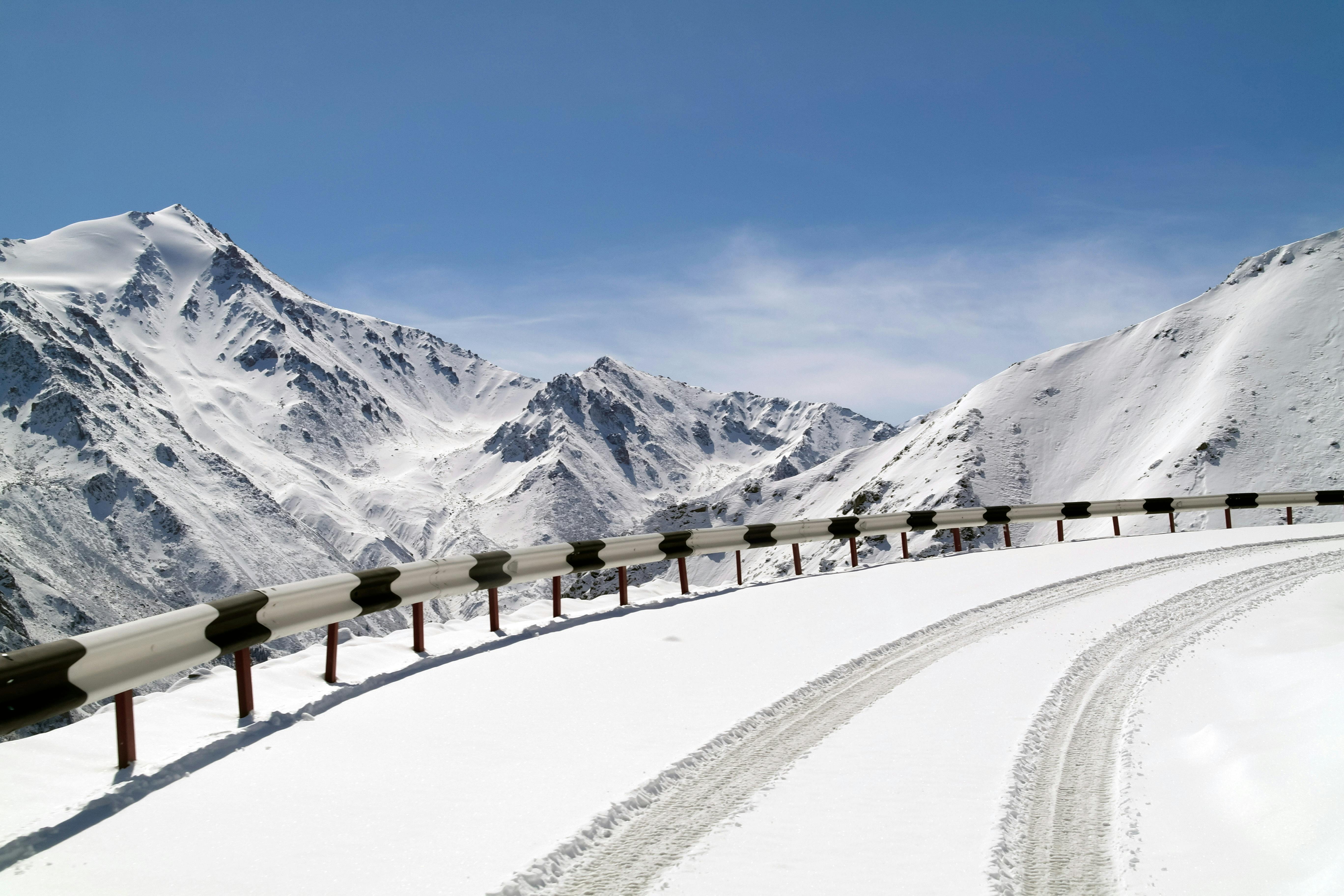 A breathtaking view of a snow-covered road winding through mountainous terrain under a clear blue sky.