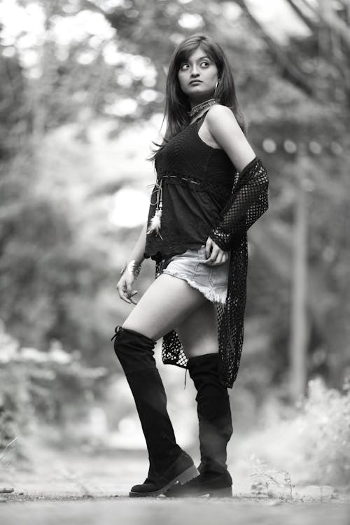 A Grayscale Photo of a Woman in Black Tank Top and Boots Posing on the Street