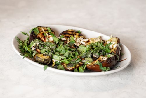 Free Appetizing grilled eggplant dish garnished with vibrant fresh herbs served on a white plate. Stock Photo