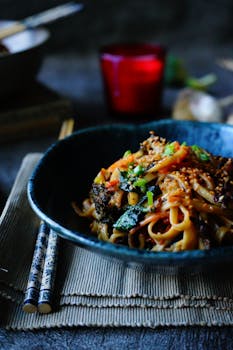 A gourmet Asian noodle dish served with vegetables and sesame seeds in a black bowl.