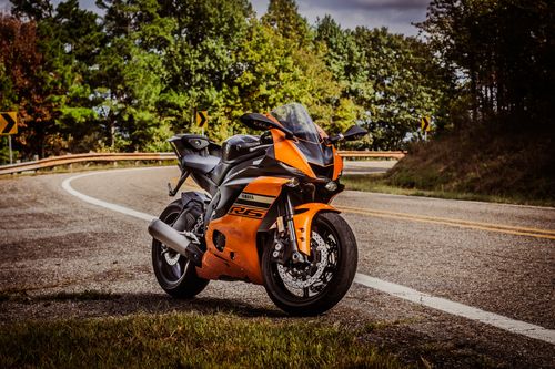 Free A vibrant orange motorcycle parked on a scenic curved road during autumn, surrounded by trees. Stock Photo