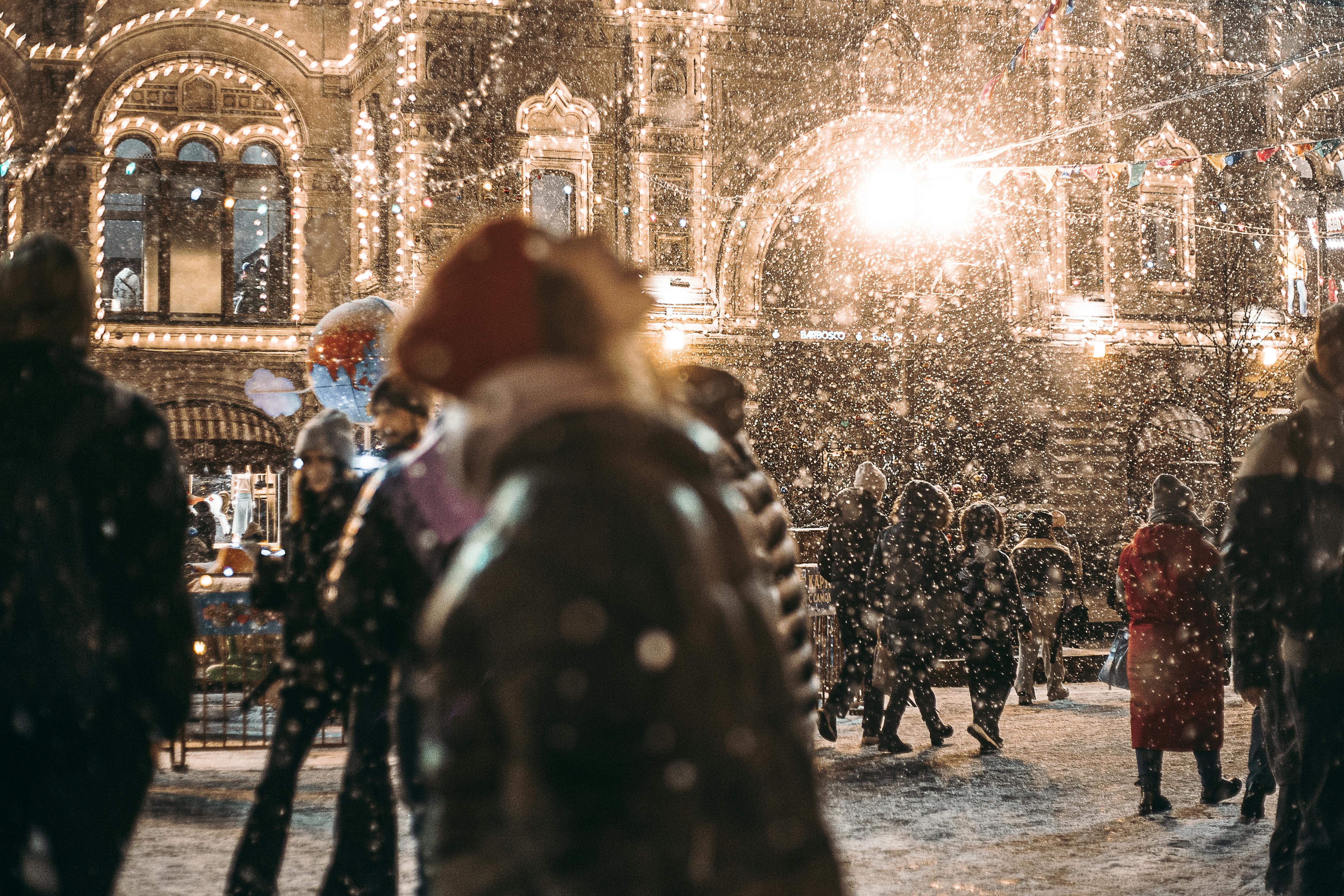 People gather on a snowy street under festive lights, capturing a cozy winter evening vibe.