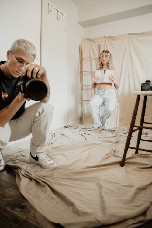 Man Holding Black Camera Beside a Woman Sitting on a Chair