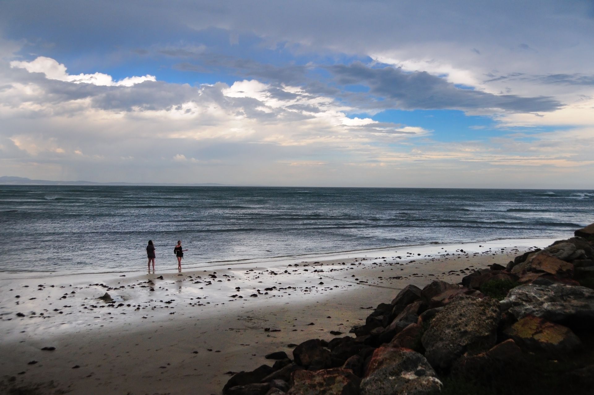 Two people walking along the shore at Jeffreys Bay, South Africa against a dramatic sky.