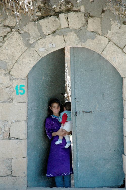 Free A young woman stands holding a baby at a rustic stone archway with a blue metal door. Stock Photo