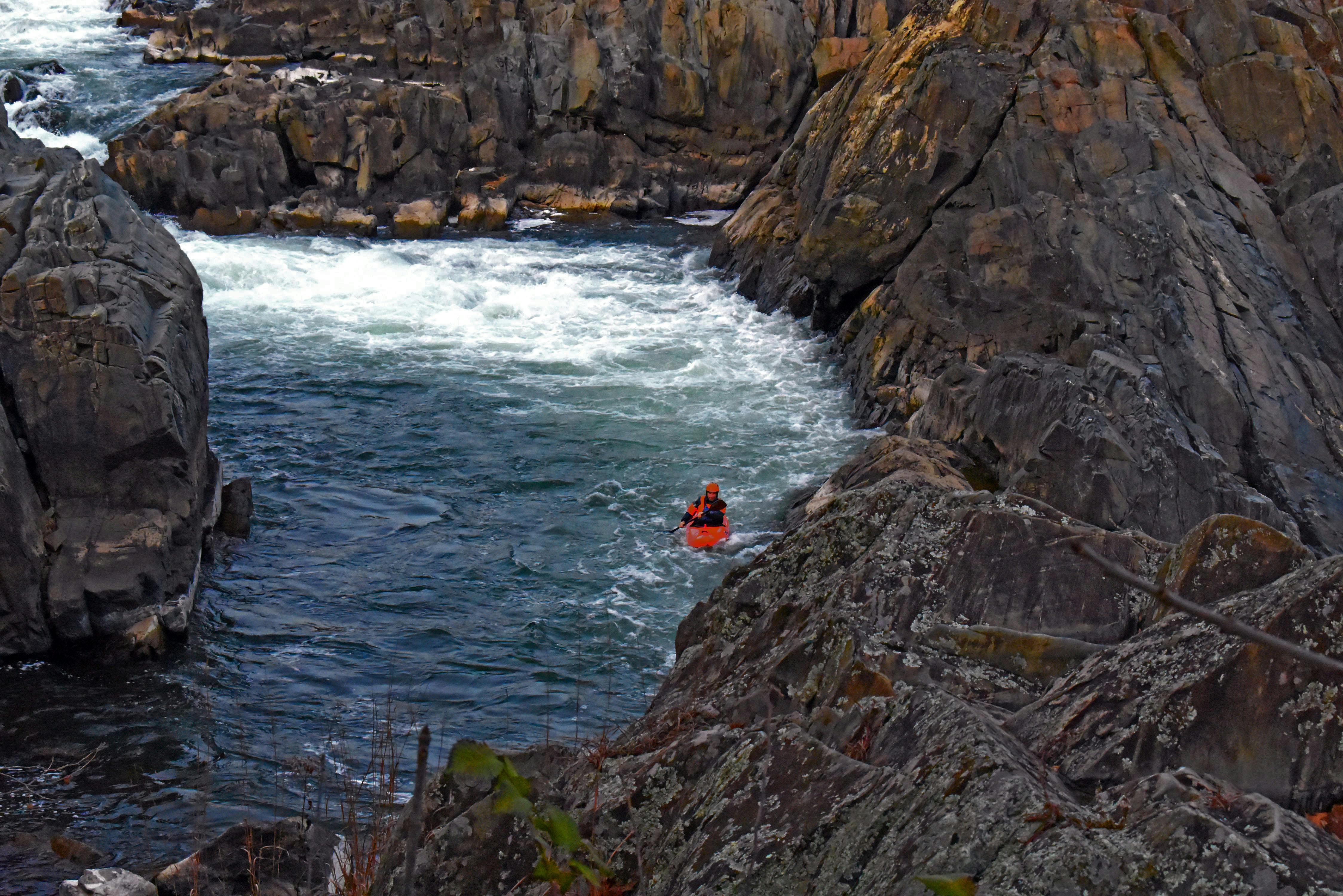 A lone kayaker skillfully navigates through rocky river rapids, surrounded by rugged cliffs.