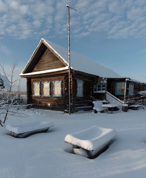 Free Charming log cabin with blue accents nestled in a snowy landscape under a clear sky. Stock Photo