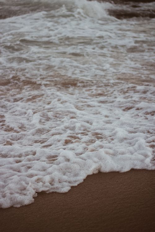 Free Close-up view of seafoam and waves gently caressing a sandy beach shoreline. Stock Photo