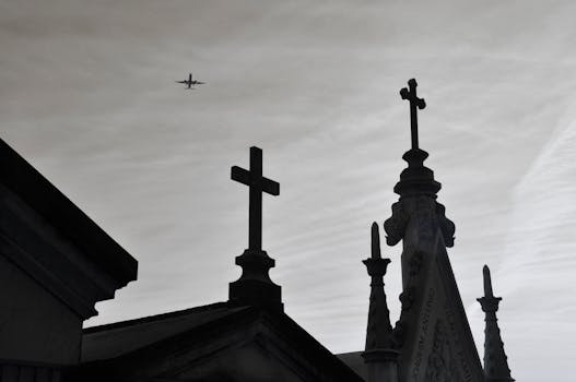 A plane flies over silhouetted crosses against a cloudy sky, capturing themes of travel and spirituality.