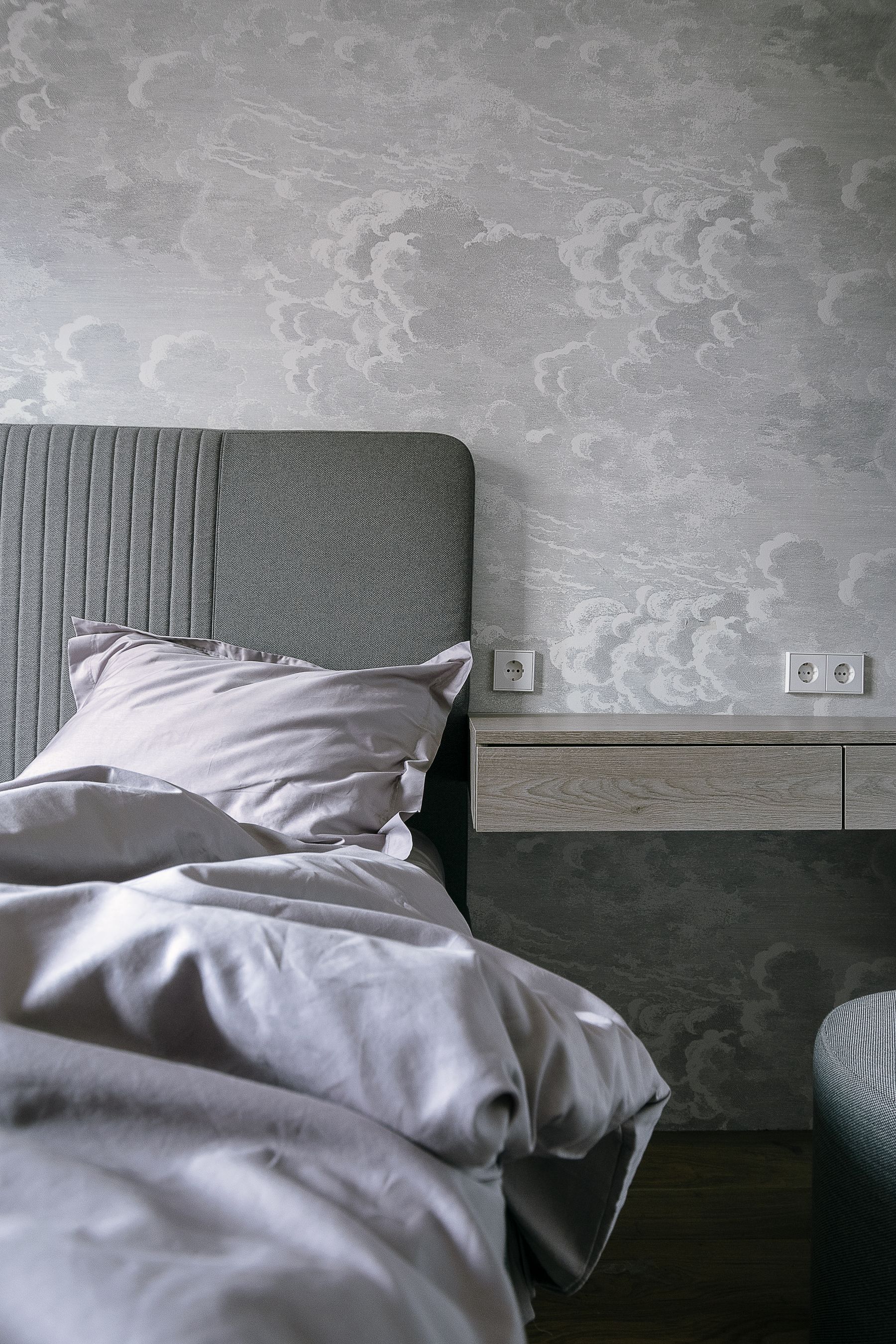 Grey-and-white bedding layered on a bed against textured grey wallpaper
