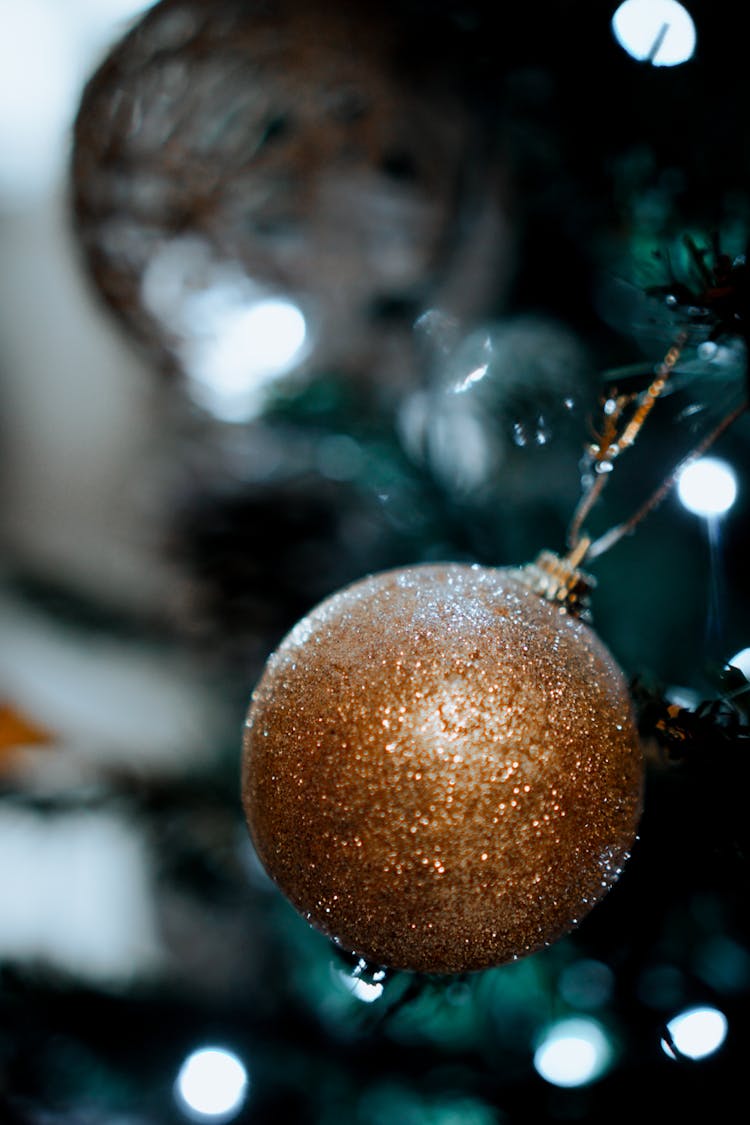 A Gold Glistening Bauble Hanging On Christmas Tree