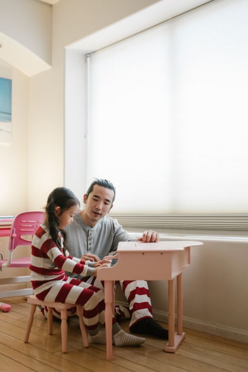 Free A father and daughter enjoying music together by playing a small toy piano indoors. Stock Photo