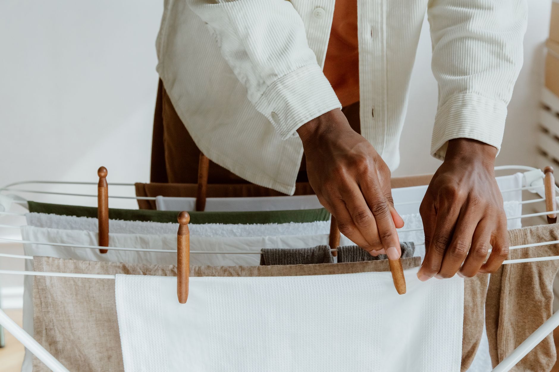 Close-up of a man hanging fresh laundry on a drying rack indoors, emphasizing cleanliness and domestic life.