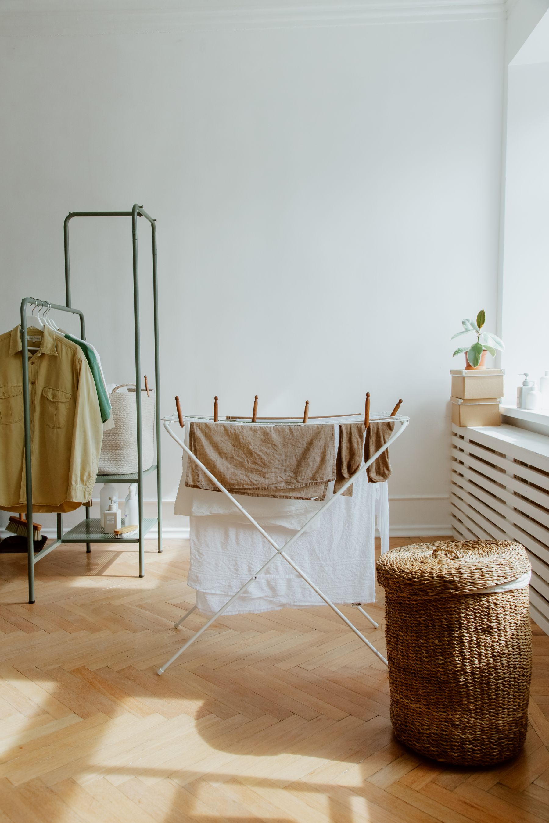 A bright organized laundry room with a wicker basket, drying rack, shelving, and folded textiles
