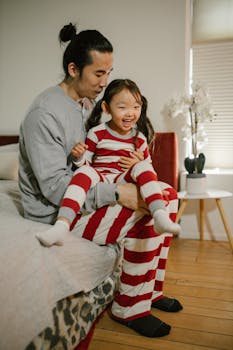 A cheerful father and daughter in striped pajamas enjoying their morning together in a cozy bedroom.