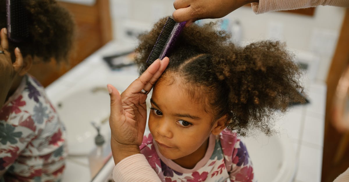 A mother styles her young daughter's hair in front of a bathroom mirror with gentle care