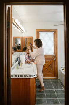 A mother styling her daughter's hair in their cozy bathroom, capturing family bonding.