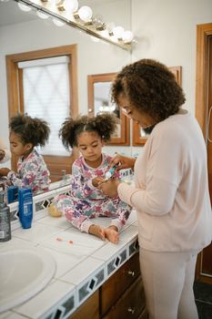 A mother helps her daughter with brushing teeth during a morning routine.
