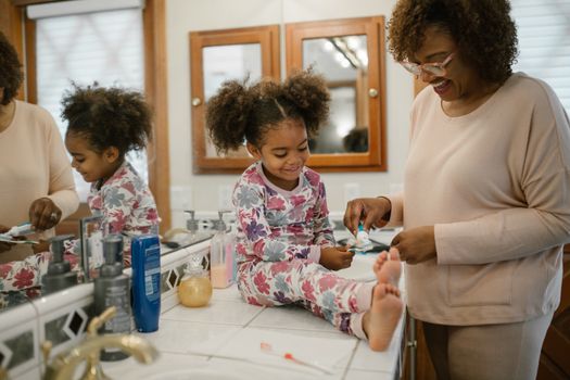 A cheerful mother and daughter enjoy a morning toothbrushing routine together in pajamas.