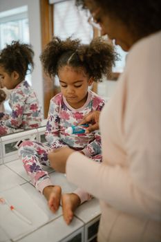 A mother helps her daughter with toothpaste during their morning routine.