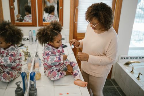 Free A parent helps a child brush teeth in a bathroom during a morning routine. Stock Photo