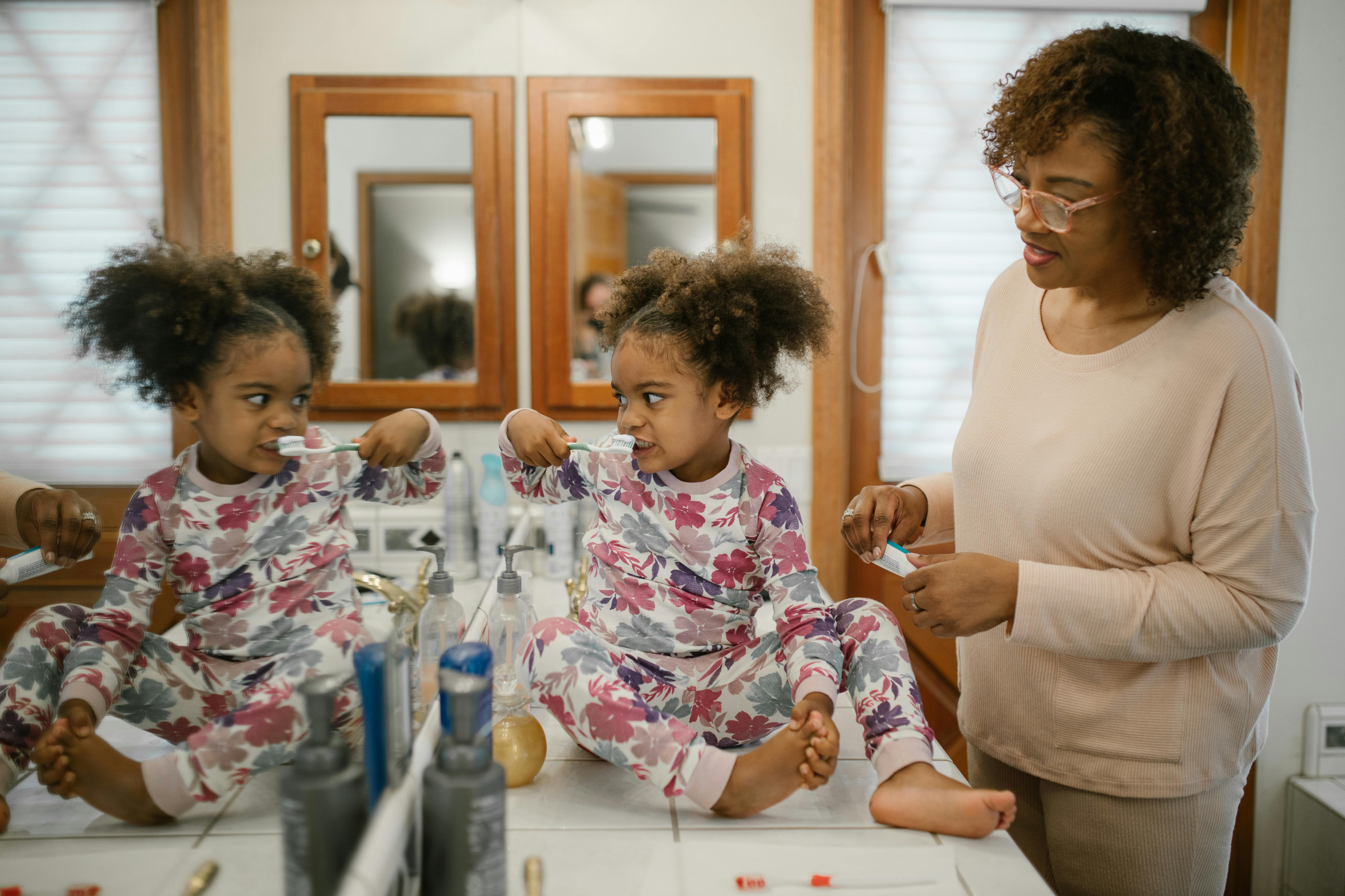 girl cleaning teeth with mother supervision