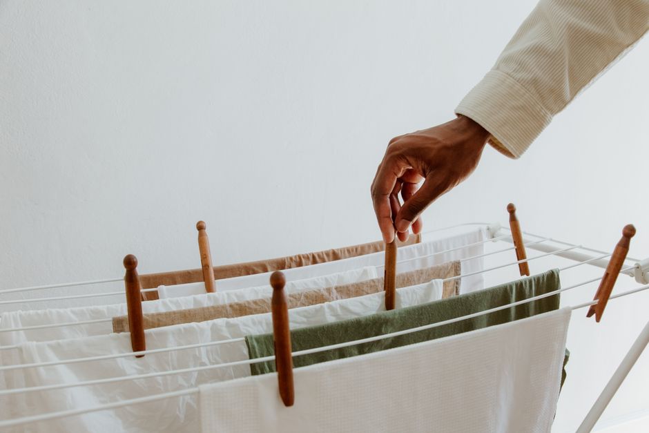 Close-up view of a hand placing clothes on a drying rack indoors, emphasizing freshness and hygiene.