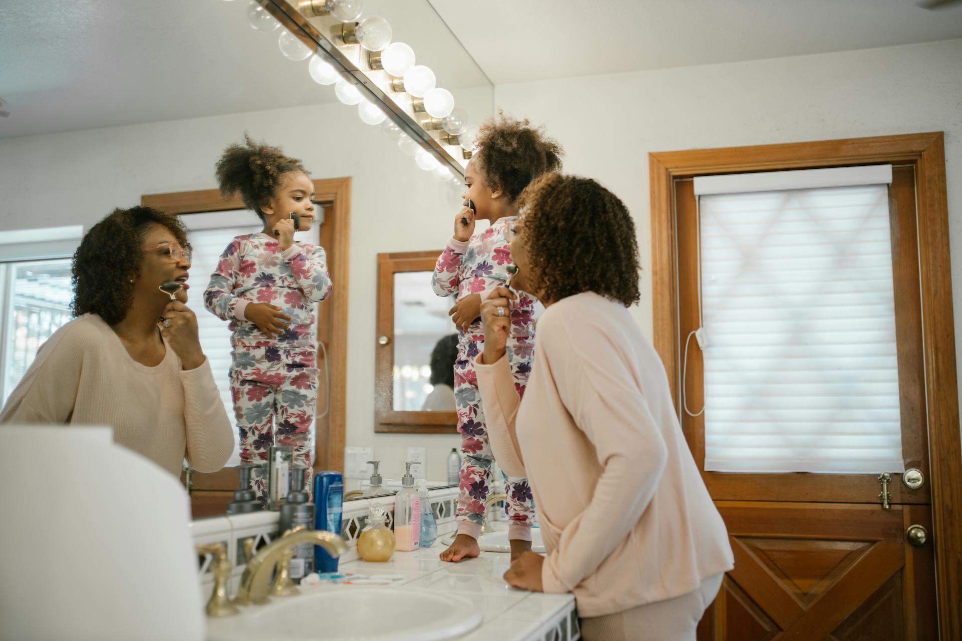 Mother and daughter sharing a joyful morning beauty routine in the bathroom.