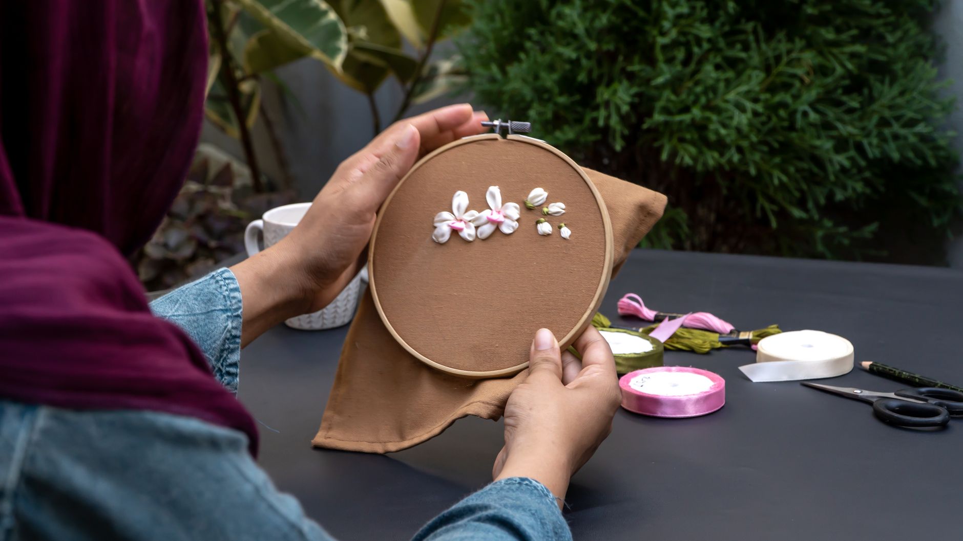 Close-up of hands working on floral embroidery in an outdoor setting.