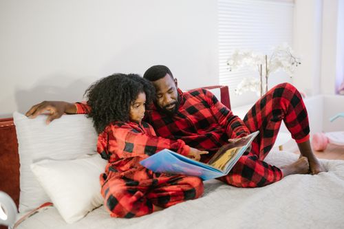 Free Father and daughter in matching pajamas reading a book together on a bed, creating a warm family moment. Stock Photo