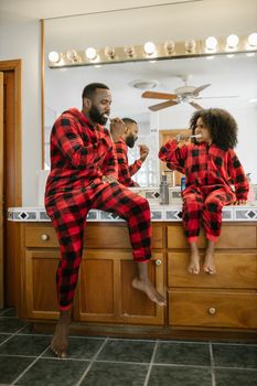 Father and daughter in pajamas brushing teeth together in the bathroom.