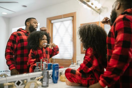 Father and daughter in matching pajamas brushing teeth, fostering bonding and hygiene.