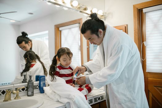 Father helping daughter brush teeth during morning bathroom routine.
