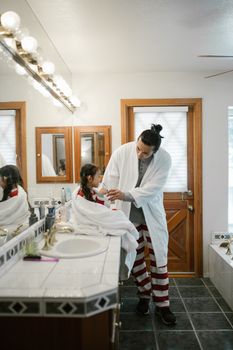 A dad helps his daughter with her morning hygiene routine in a cozy bathroom setting.