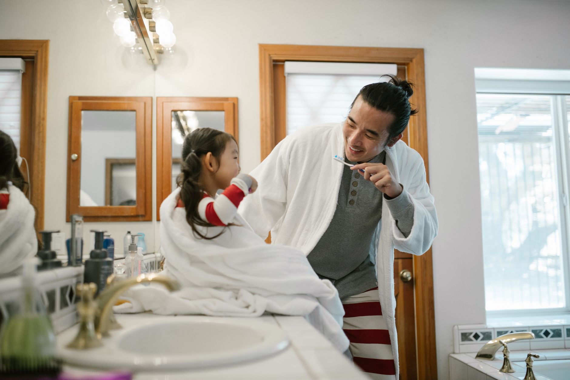 A father and daughter brush their teeth together, practicing good hygiene in the bathroom.