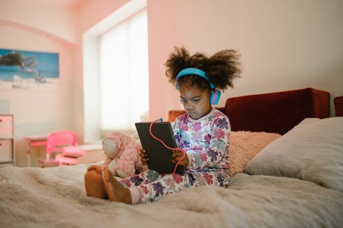 Free Child Sitting on Bed with Tablet Stock Photo