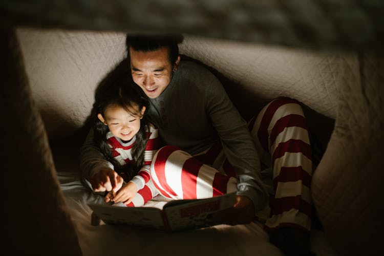 Father With Daughter Reading Book Under Blanket