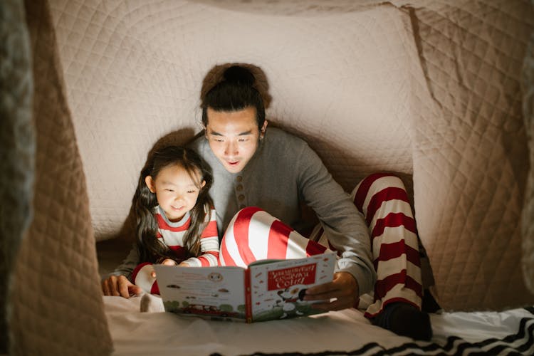 Daughter Reading Book With Father Using Light