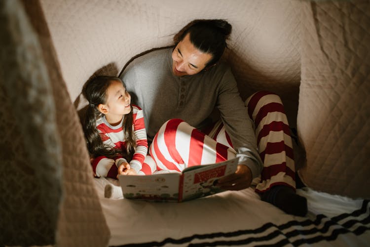 Father With Daughter Under Blanket Reading Book