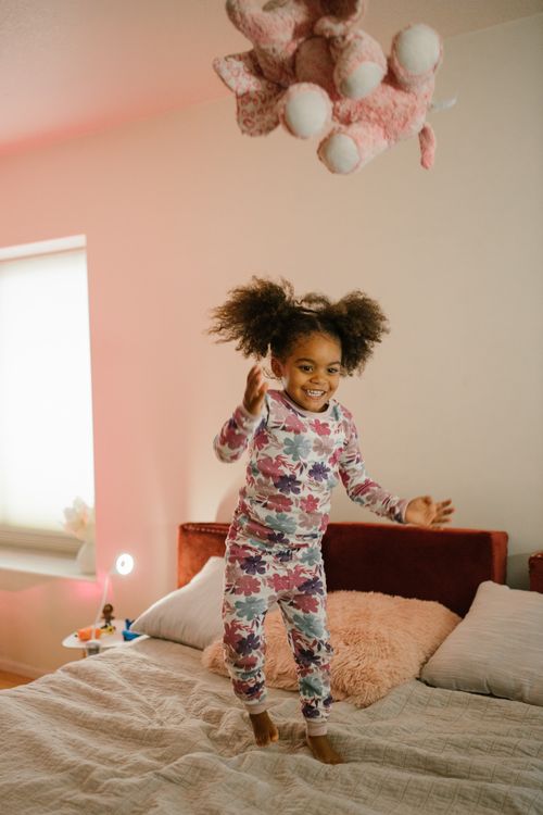 Free A happy child in pajamas jumping on a bed in a cozy, sunlit bedroom. Stock Photo