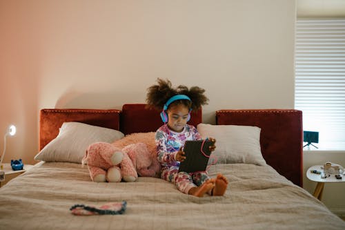 Free Little Girl Using Tablet in Bed Stock Photo