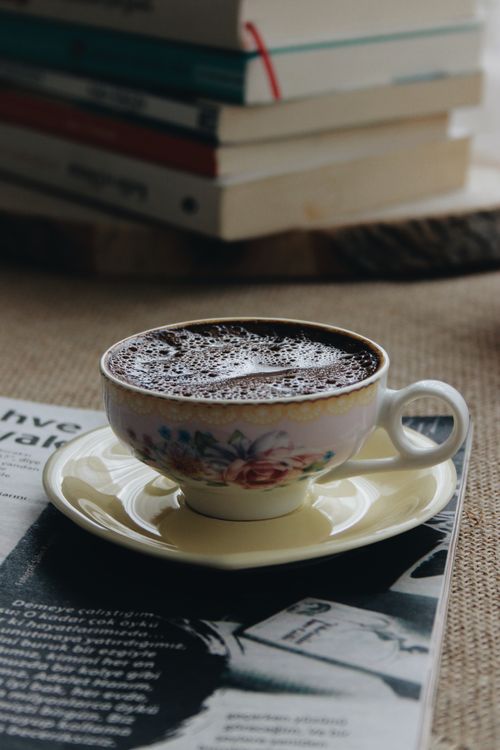 Free A decorative porcelain coffee cup sits on a magazine next to a stack of books. Stock Photo