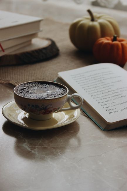 A cozy autumn scene with a coffee cup, open book, and pumpkins on a table indoors.