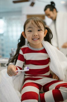 A smiling young girl in striped pajamas holding a toothbrush, ready for bedtime.