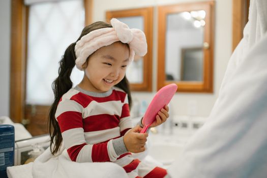 Happy child with headband playing with a hairbrush in a cozy bathroom setting.