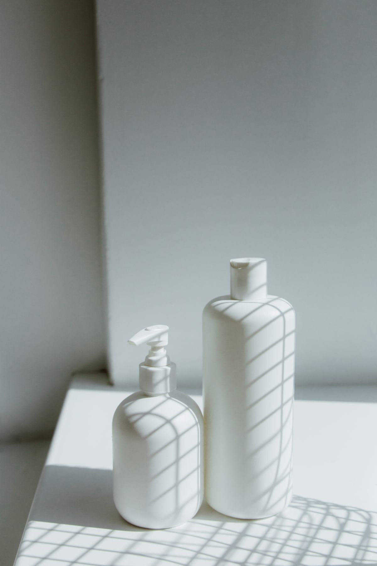 Two unlabelled white bottles on a sunlit shelf with window shadows
