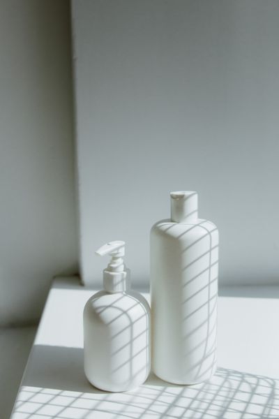 Two unlabelled white bottles on a sunlit shelf with window shadows