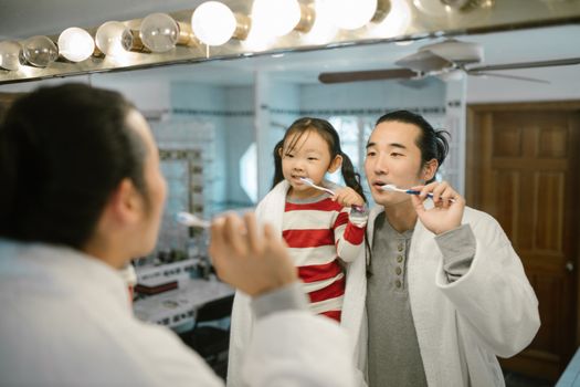 A father and daughter bonding while brushing teeth in the bathroom mirror.