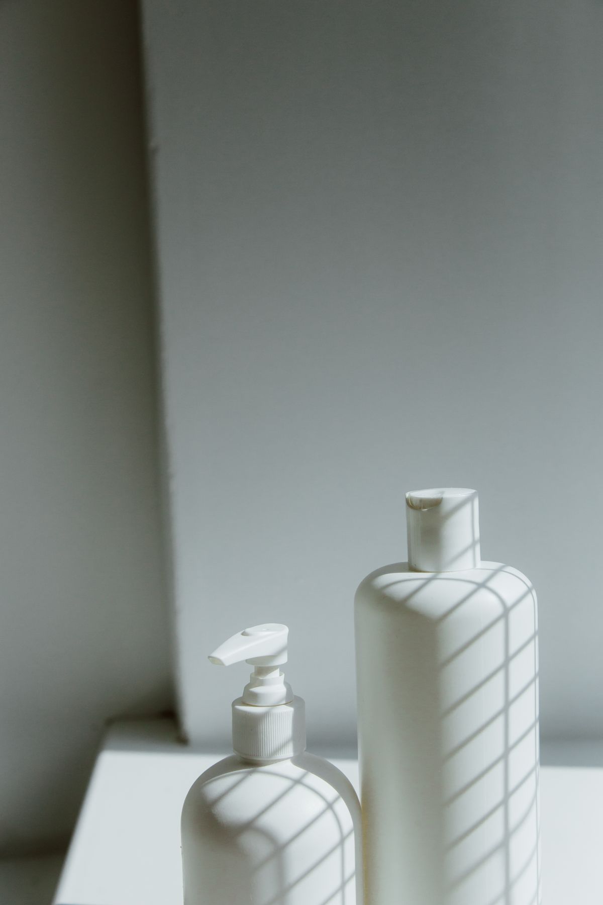 Minimalist photo of white plastic bottles with geometric shadow patterns, ideal for product focus.